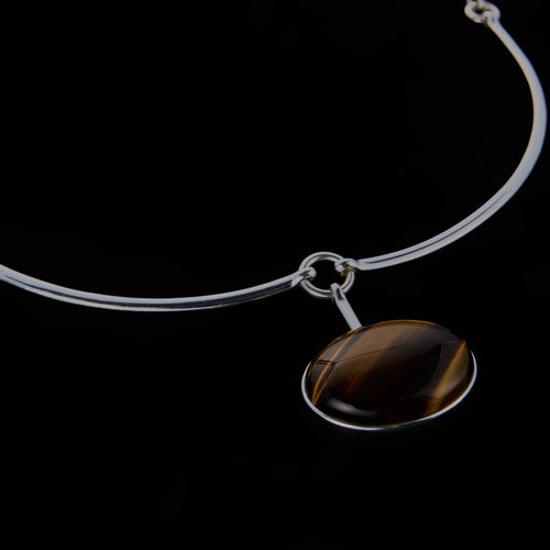 A modernist 925 silver necklace featuring a rigid frontal arc, hidden articulated chain, and a suspended Tiger Eye cabochon. Architectural jewelry by Saël.