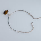 A modernist 925 silver necklace featuring a rigid frontal arc, hidden articulated chain, and a suspended Tiger Eye cabochon. Architectural jewelry by Saël.